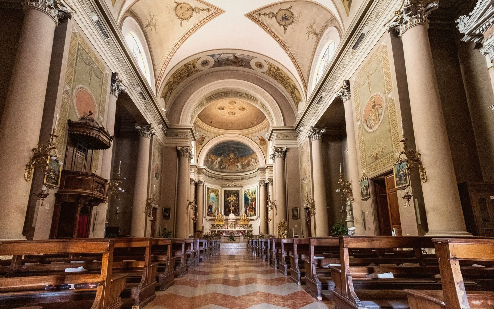 Empty church nave with wooden pews leading to a domed, frescoed altar area