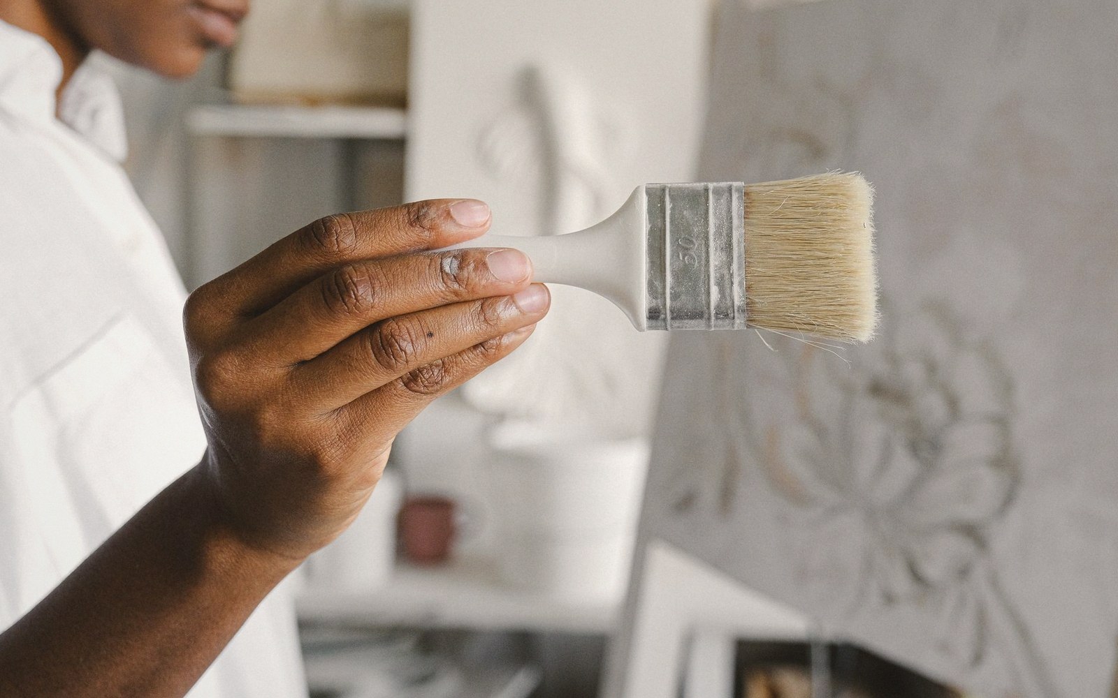 A hand holds a wide bristle brush near a textured plaster surface